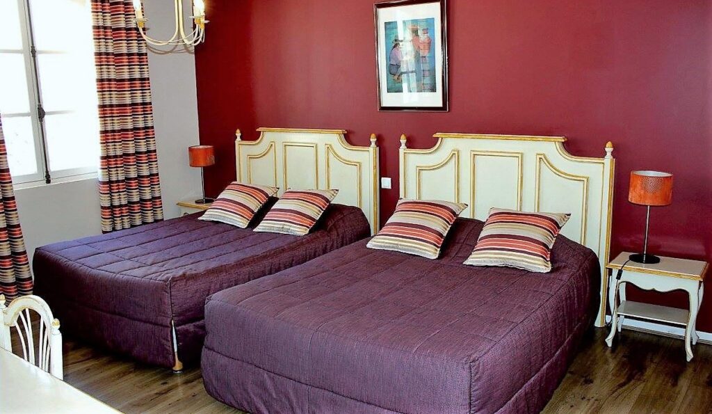 Chambre double avec murs bordeaux, draps pourpres et détails dorés, avec une touche provençale.