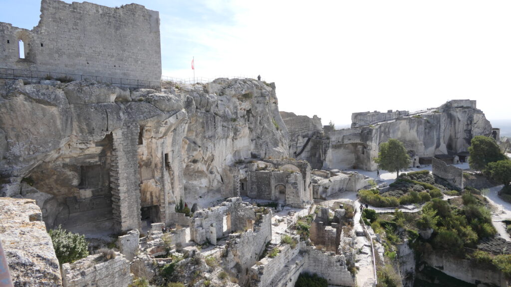 Ruines et structures en pierre du Château des Baux-de-Provence avec le drapeau français flottant au sommet d'une tour.