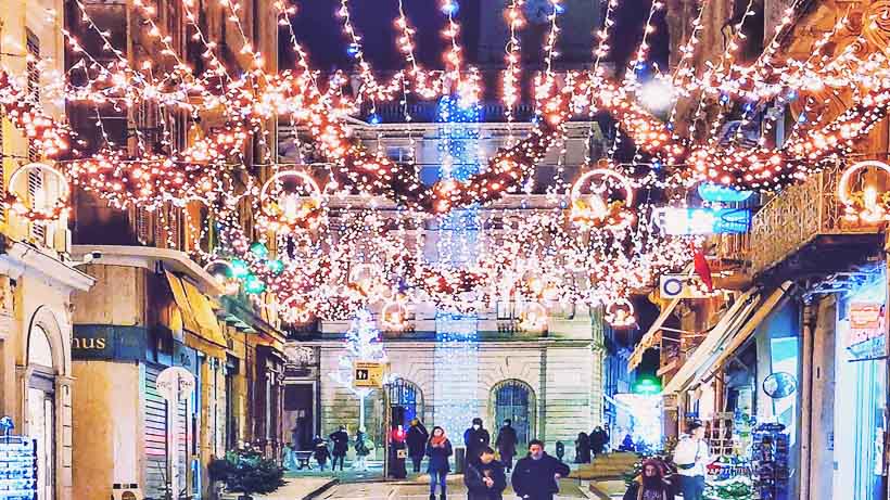 Illuminations de Noël scintillant dans une rue animée d'Arles, avec des piétons profitant de l'atmosphère festive.