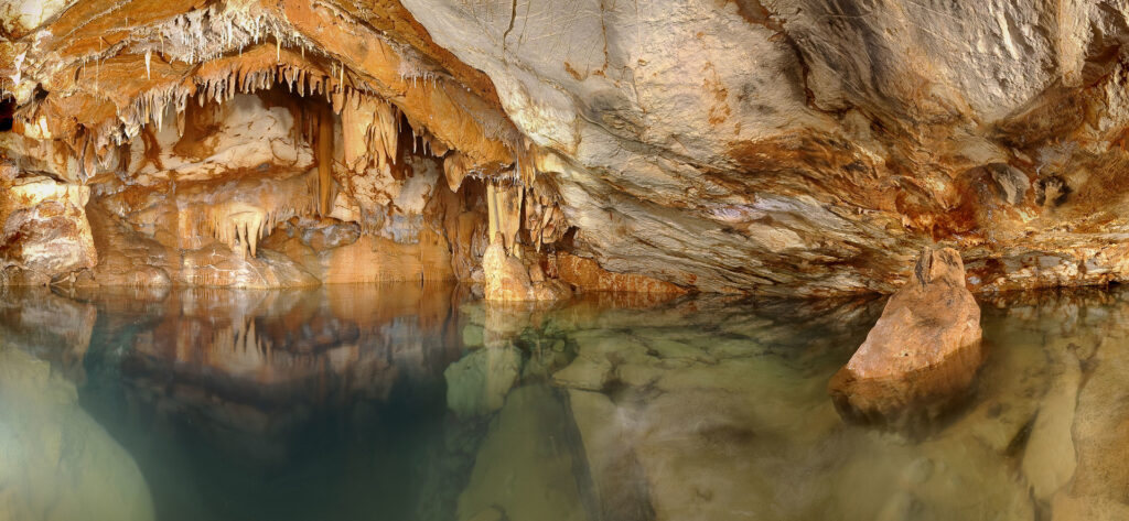 Vue générale du puits avec draperie des mains noires et mains noires sur la paroi dans la Grotte Cosquer Marseille, montrant des formations géologiques et des stalactites.